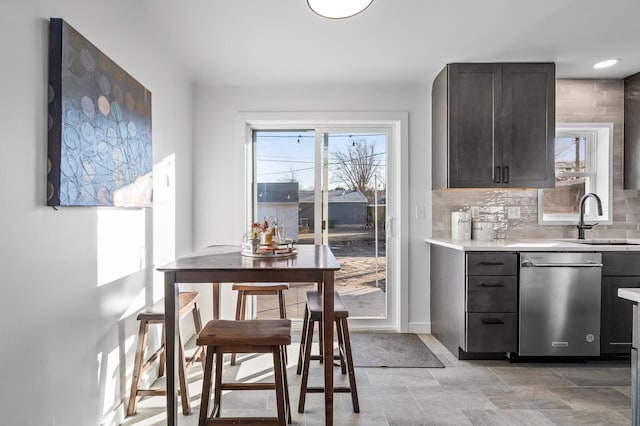 kitchen with baseboards, a sink, light countertops, dishwasher, and tasteful backsplash