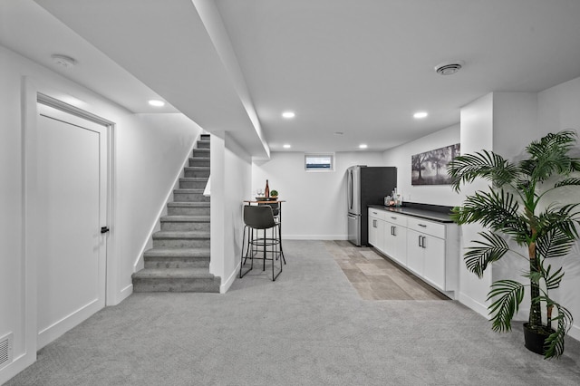 bar with visible vents, light colored carpet, a bar, and freestanding refrigerator