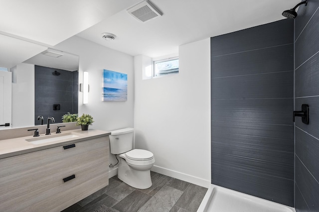 bathroom featuring visible vents, toilet, a tile shower, baseboards, and vanity