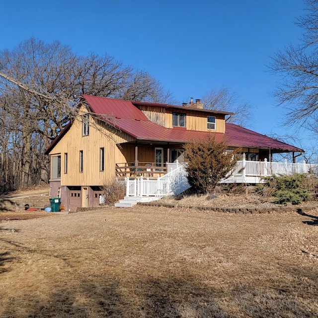 rear view of house with a porch, a chimney, an attached garage, and metal roof