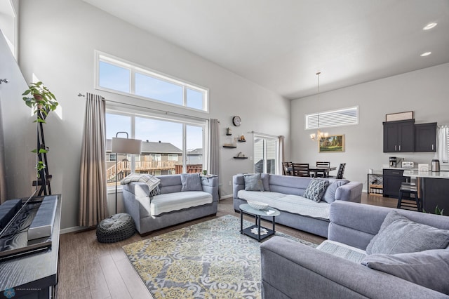 living room with wood finished floors, a towering ceiling, recessed lighting, baseboards, and a chandelier