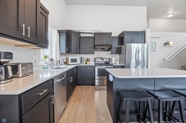 kitchen featuring stainless steel appliances, light wood-style floors, exhaust hood, a breakfast bar area, and light countertops