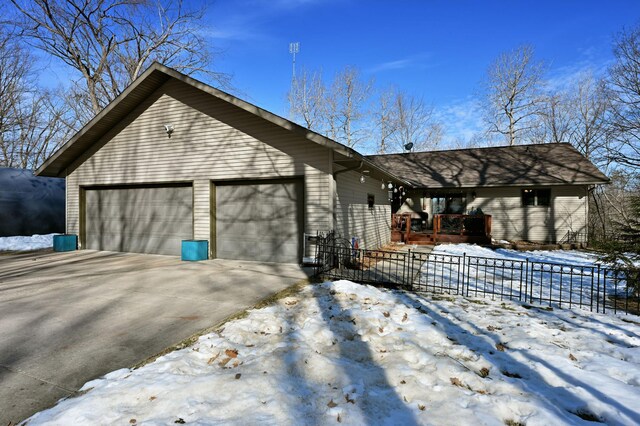 view of snow covered exterior featuring an attached garage, fence, and driveway