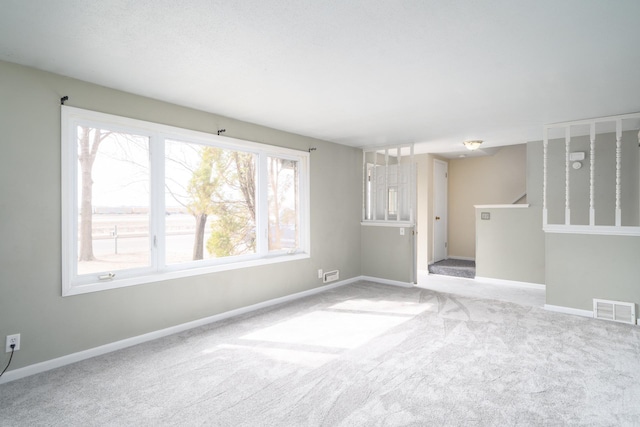 carpeted spare room featuring stairway, baseboards, and visible vents