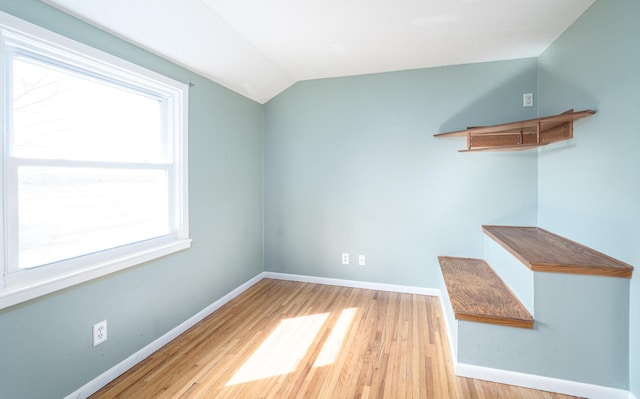 empty room featuring vaulted ceiling, baseboards, and wood finished floors