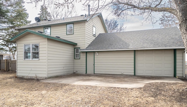 back of house with an attached garage, driveway, roof with shingles, and fence