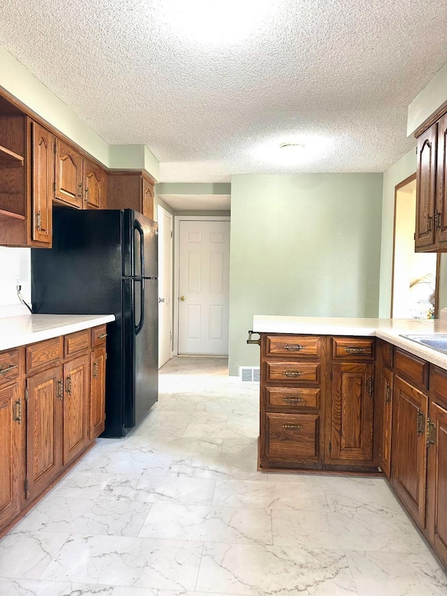 kitchen featuring light countertops, a peninsula, freestanding refrigerator, marble finish floor, and open shelves