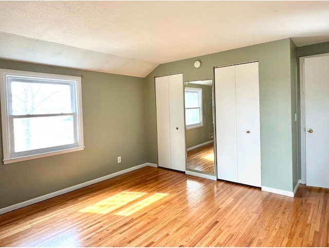 unfurnished bedroom with baseboards, multiple closets, vaulted ceiling, light wood-style floors, and a textured ceiling