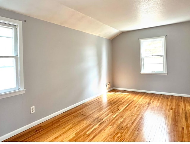 spare room with lofted ceiling, light wood-style flooring, and baseboards