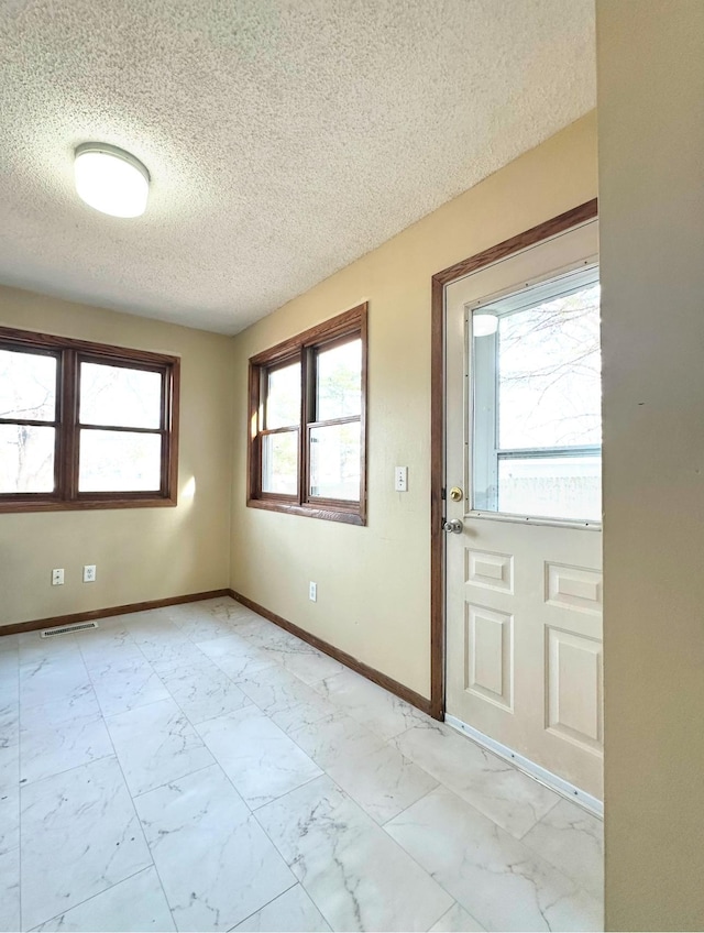 doorway with visible vents, marble finish floor, a textured ceiling, and baseboards