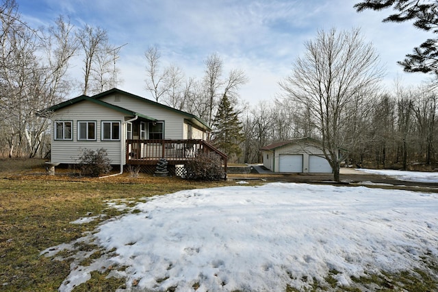 view of snow covered exterior featuring an outdoor structure, a detached garage, and a wooden deck