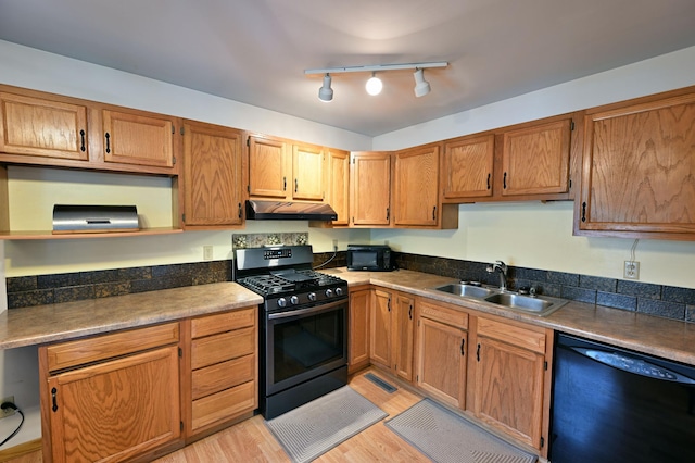 kitchen with light wood-type flooring, a sink, black appliances, under cabinet range hood, and brown cabinets