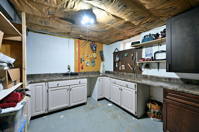 kitchen with white cabinetry, open shelves, dark countertops, and concrete flooring