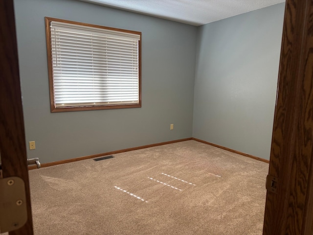 carpeted empty room with baseboards, visible vents, and a textured ceiling