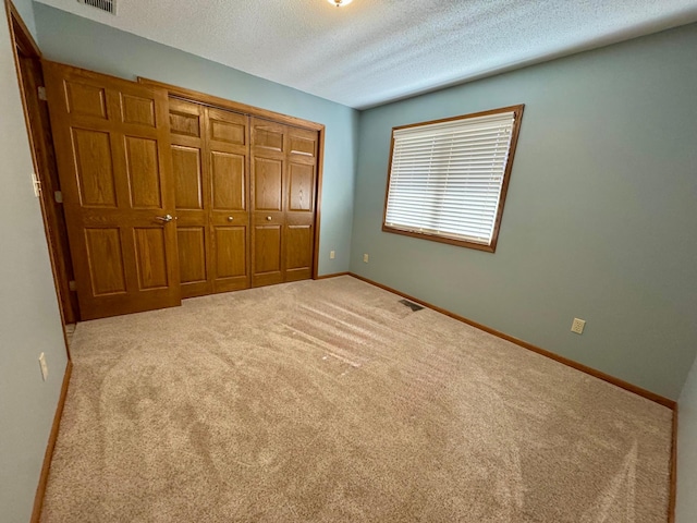 unfurnished bedroom with visible vents, a textured ceiling, a closet, carpet floors, and baseboards