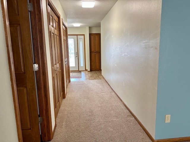 hallway featuring light colored carpet, a textured ceiling, baseboards, and a textured wall