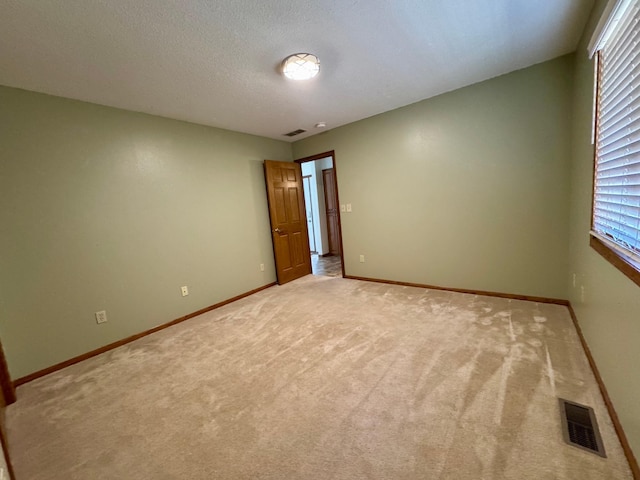 empty room with light colored carpet, baseboards, visible vents, and a textured ceiling