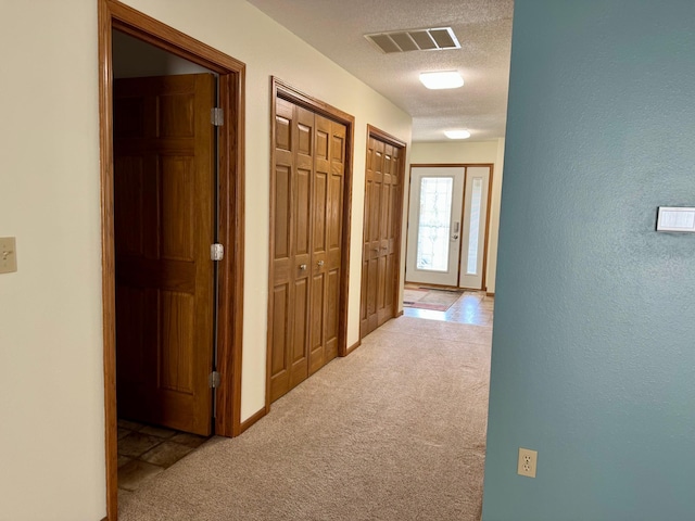 hall featuring visible vents, a textured ceiling, carpet, and a textured wall