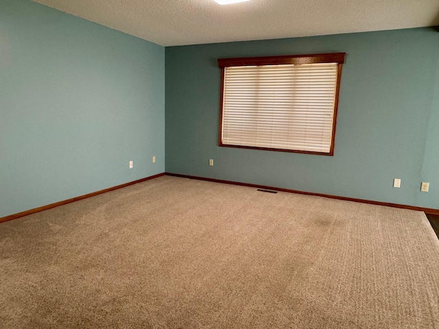 carpeted empty room featuring a textured ceiling and baseboards