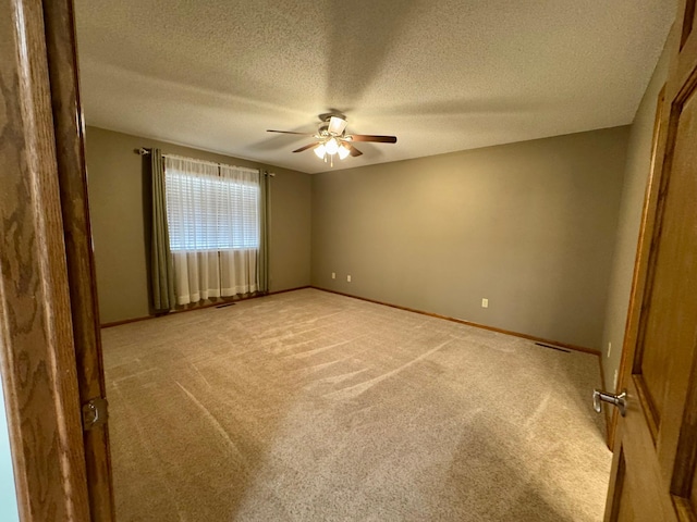 spare room with light colored carpet, a textured ceiling, baseboards, and a ceiling fan