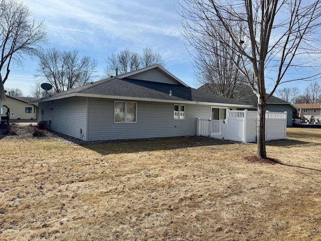 back of house with a yard, a shingled roof, and fence