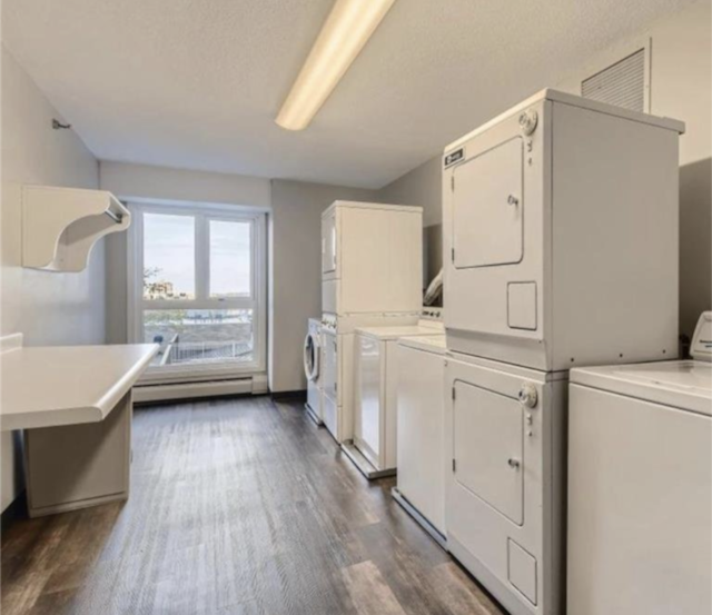 shared laundry area with washer and dryer, a baseboard heating unit, dark wood-style flooring, and stacked washing maching and dryer