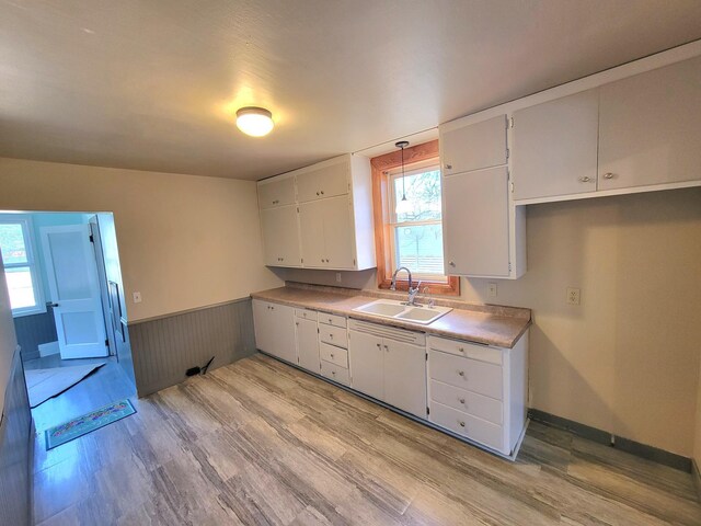 kitchen with light wood finished floors, a sink, white cabinets, wainscoting, and light countertops