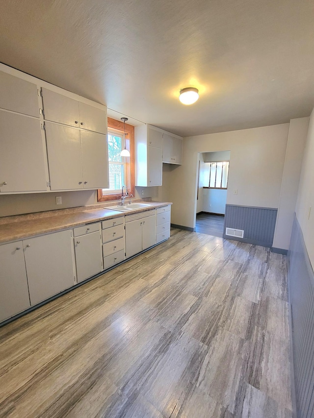 kitchen with visible vents, light wood finished floors, a sink, light countertops, and white cabinets
