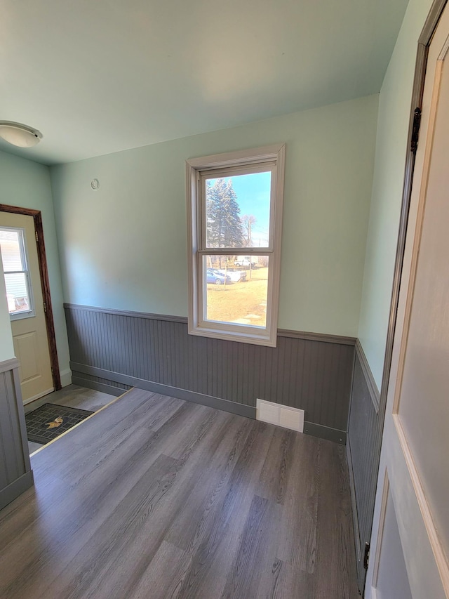 spare room with a wealth of natural light, a wainscoted wall, and wood finished floors