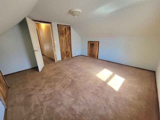 additional living space with visible vents, baseboards, carpet flooring, and vaulted ceiling