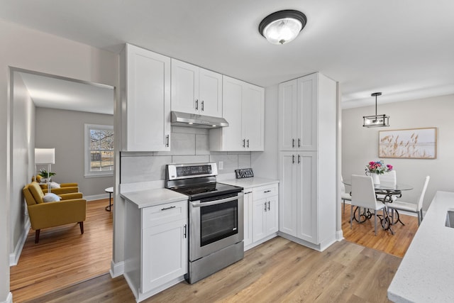 kitchen with tasteful backsplash, under cabinet range hood, stainless steel electric stove, light countertops, and light wood-style floors