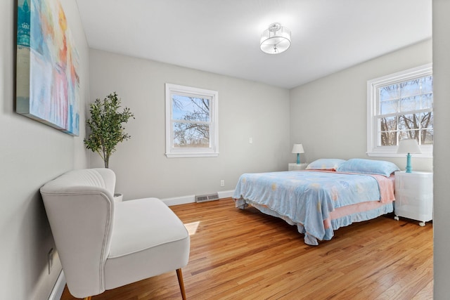 bedroom featuring baseboards, multiple windows, visible vents, and light wood-style flooring