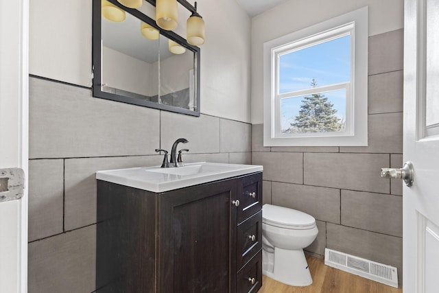 half bath featuring visible vents, toilet, vanity, and tile walls