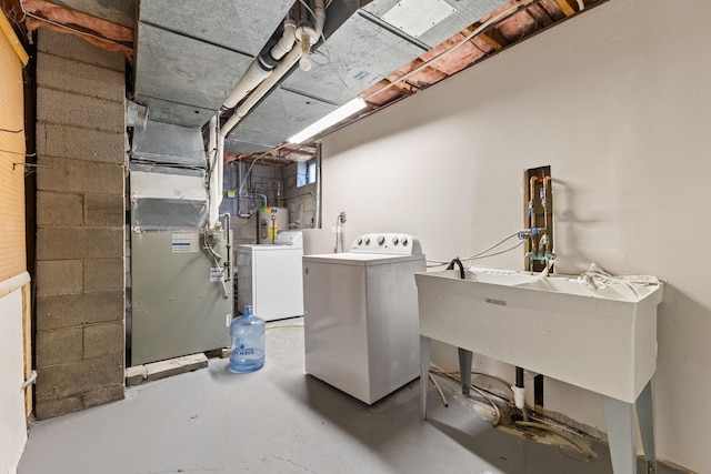 clothes washing area featuring heating unit, concrete block wall, laundry area, water heater, and washing machine and dryer