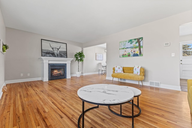 living room with a glass covered fireplace, light wood-style floors, visible vents, and baseboards