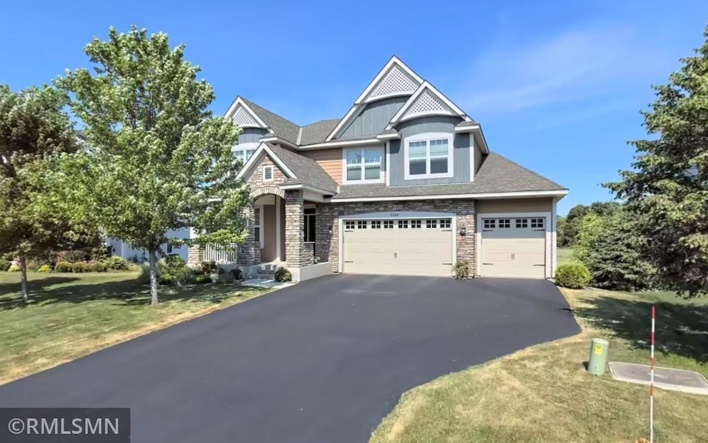 view of front of property featuring aphalt driveway, a garage, stone siding, and a front yard