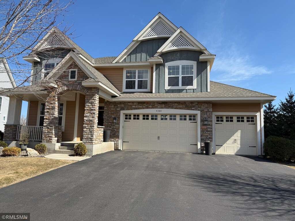 view of front facade featuring board and batten siding, a porch, a garage, stone siding, and driveway