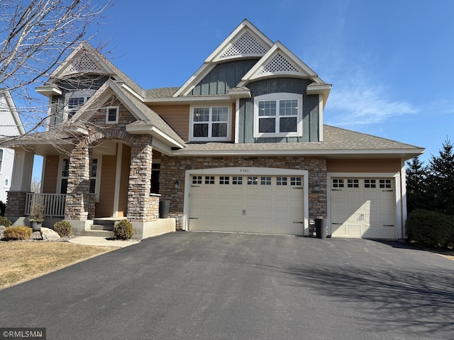 view of front facade featuring board and batten siding, a porch, a garage, stone siding, and driveway
