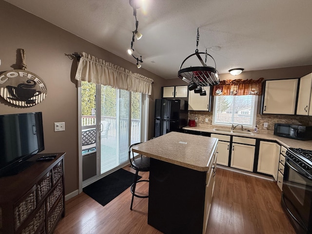 kitchen featuring black appliances, a sink, dark wood-style floors, a center island, and light countertops