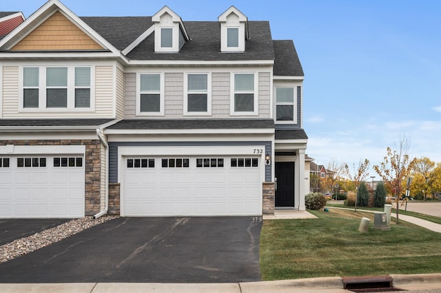 view of front of house featuring aphalt driveway, stone siding, a front yard, and an attached garage