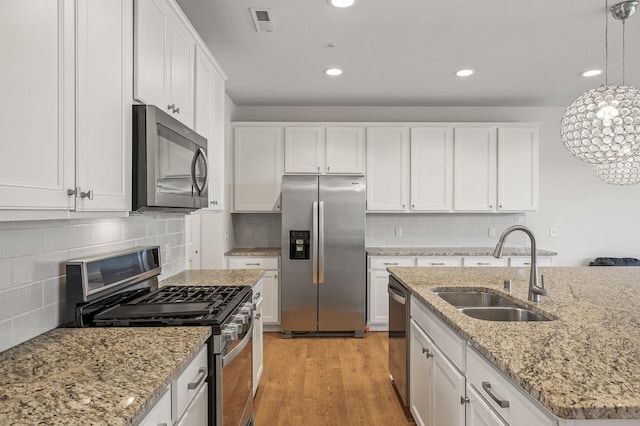 kitchen with pendant lighting, light wood-style flooring, a sink, white cabinetry, and appliances with stainless steel finishes