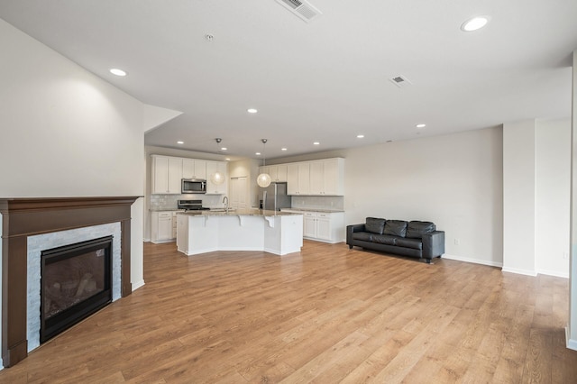 unfurnished living room featuring visible vents, baseboards, recessed lighting, light wood-style flooring, and a glass covered fireplace