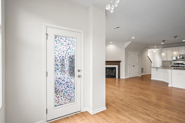 entrance foyer featuring visible vents, baseboards, a glass covered fireplace, and light wood finished floors