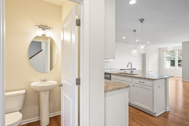 kitchen featuring white cabinetry, light stone countertops, light wood-type flooring, and a sink