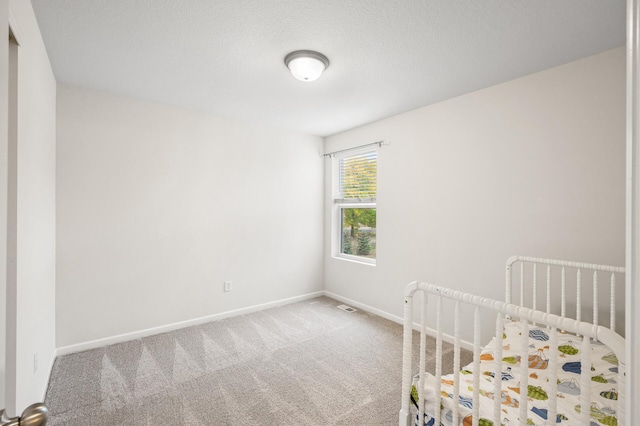 unfurnished bedroom with visible vents, a textured ceiling, a nursery area, carpet flooring, and baseboards