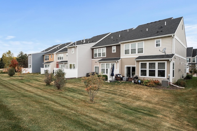 back of property featuring central air condition unit, a lawn, a shingled roof, and a residential view