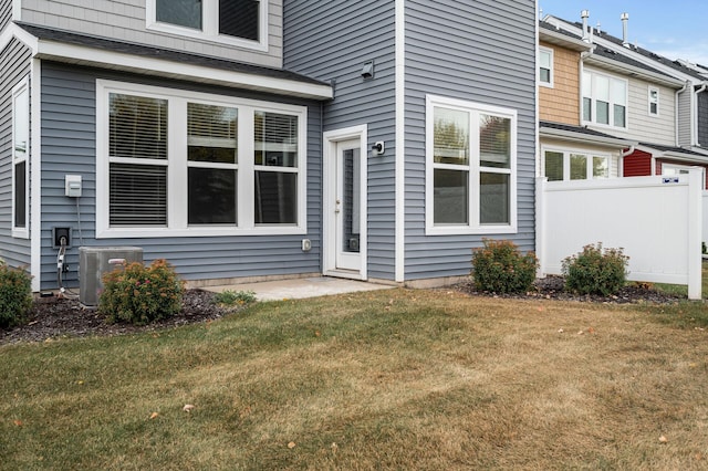 rear view of property featuring central air condition unit, a lawn, and fence