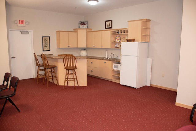 kitchen with open shelves, a breakfast bar, white appliances, dark colored carpet, and a sink