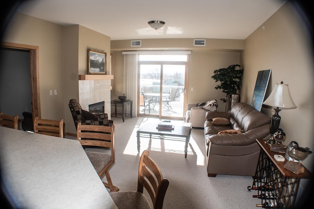 living area with a tiled fireplace, visible vents, and carpet floors