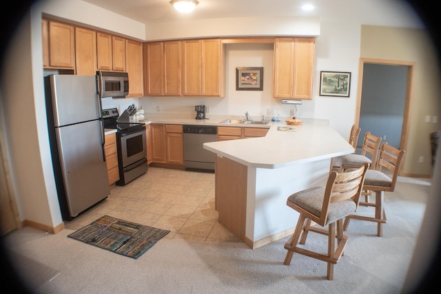 kitchen featuring a sink, appliances with stainless steel finishes, a breakfast bar area, a peninsula, and light countertops
